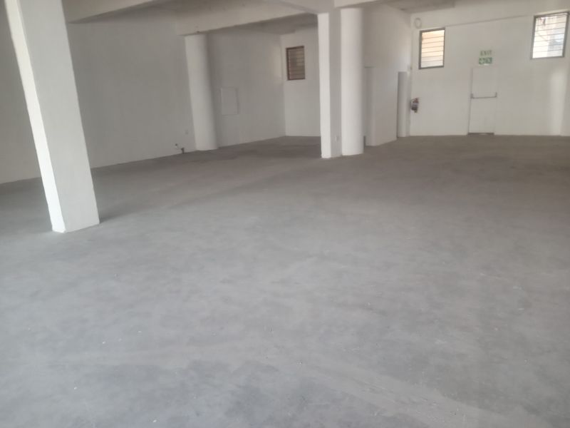 A spacious, open-plan retail unit featuring concrete flooring, structural support columns, and a designated emergency exit door.