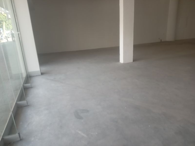 An open-plan retail space featuring polished concrete flooring, large glass storefront windows, and a structural support column.