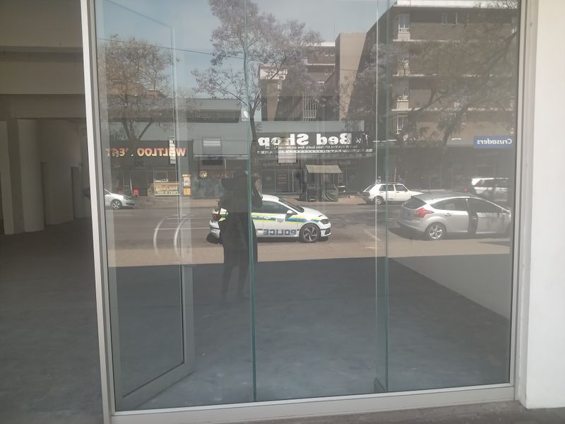 A view through a large glass storefront window looking out onto a street with parked vehicles and surrounding commercial buildings.