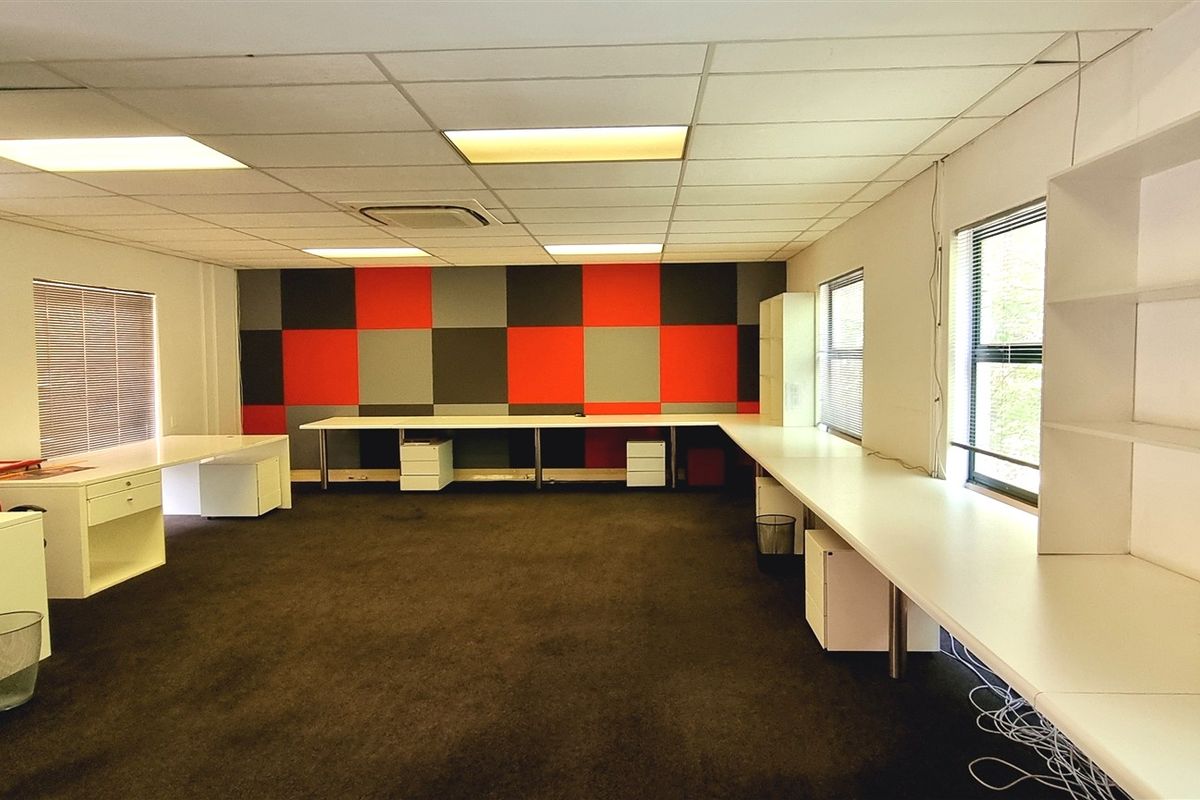 Spacious office area featuring built-in desks, integrated shelving, acoustic wall paneling, and a suspended ceiling with recessed lighting.