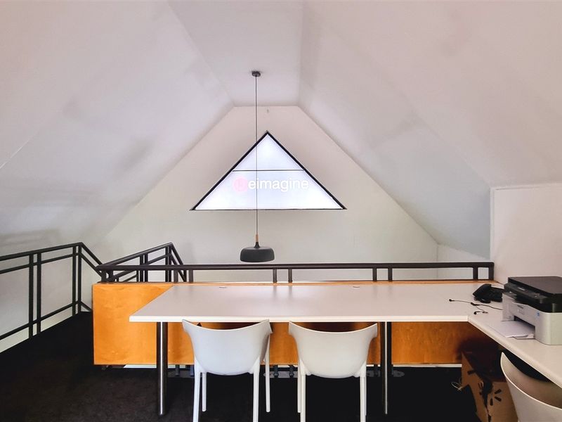 A bright attic-style office space featuring a built-in desk, metal balustrade, and a unique triangular window, providing a functional workspace.