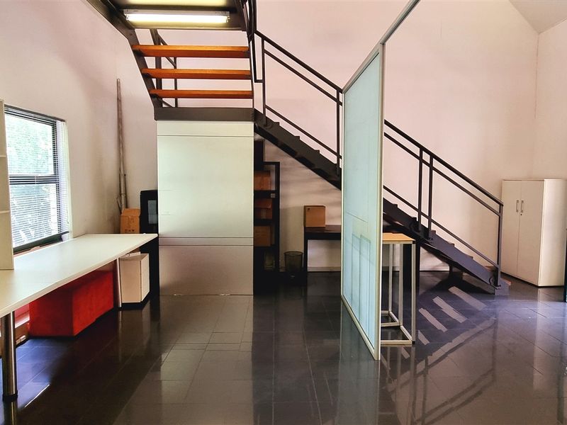 Spacious office area featuring a modern metal staircase, built-in shelving, glass partition, and polished tiled flooring in a bright, open-plan layout.