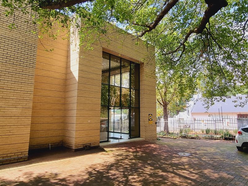 Front exterior view of the office building featuring a modern brick facade, large glass entrance, and paved driveway area.