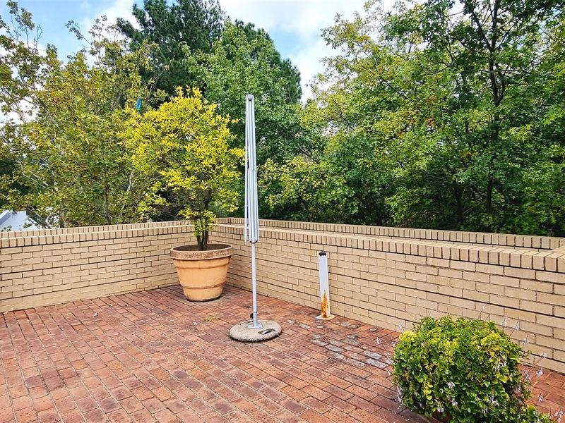 An outdoor patio area featuring brick paving and a low brick boundary wall, surrounded by mature trees.