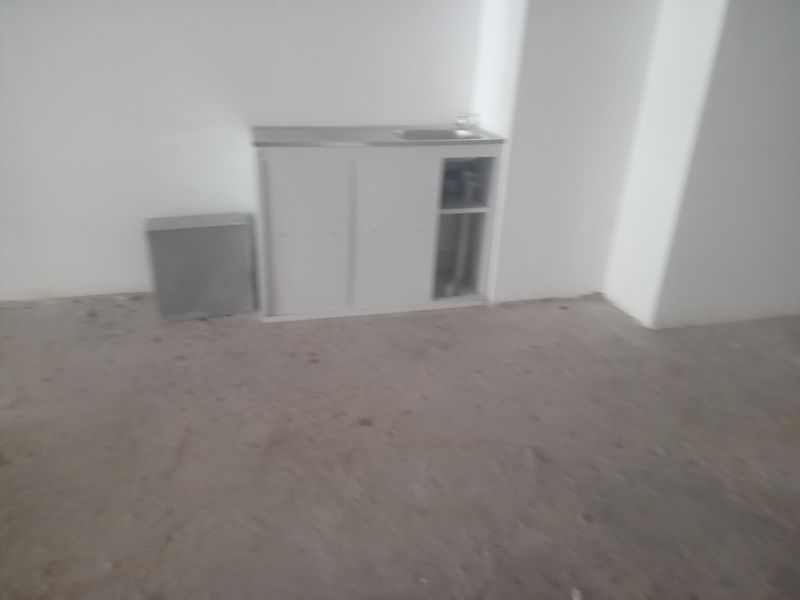 A basic kitchenette area featuring a simple sink unit with cabinetry, set within an unfinished space with exposed concrete flooring.