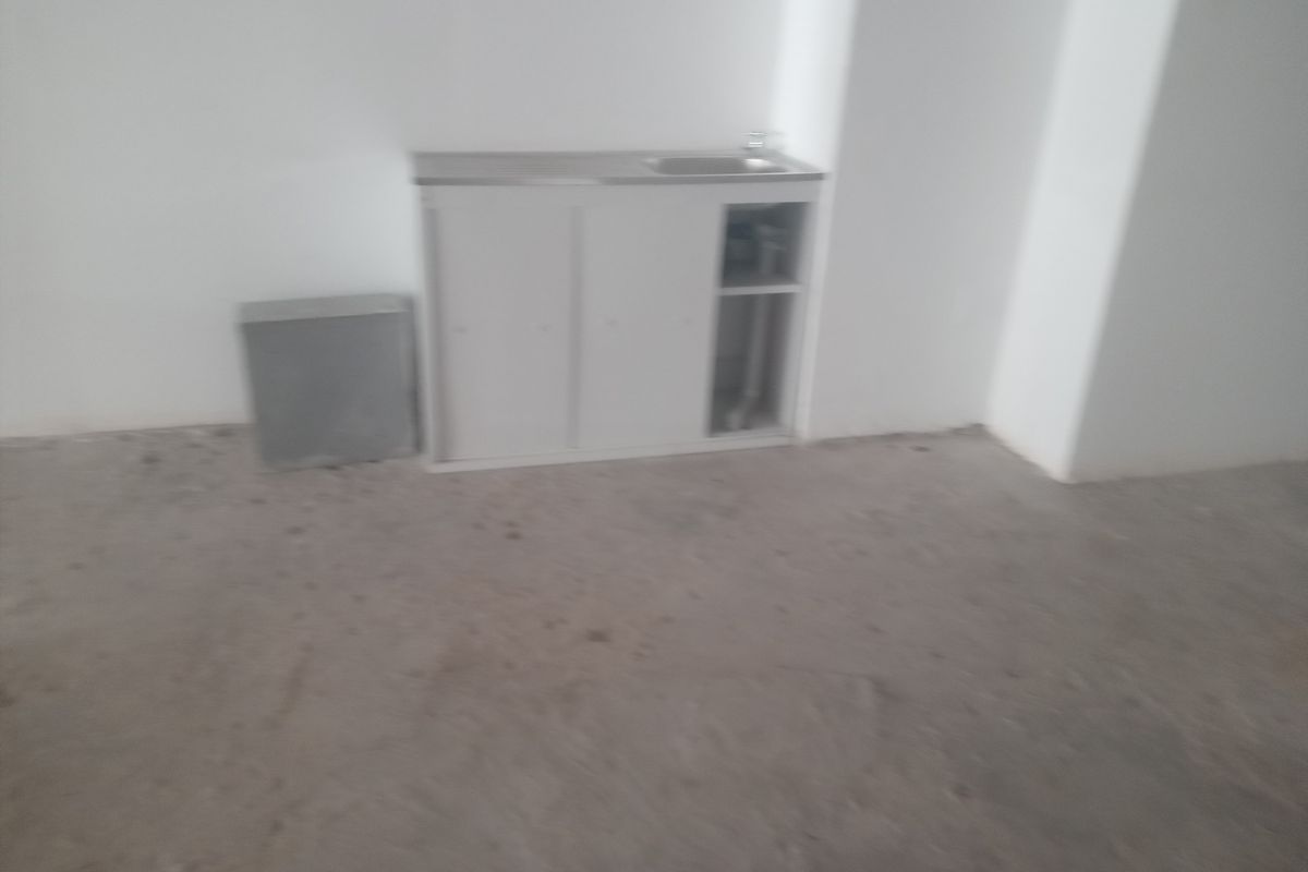 A basic kitchenette area featuring a simple sink unit with cabinetry, set within an unfinished space with exposed concrete flooring.
