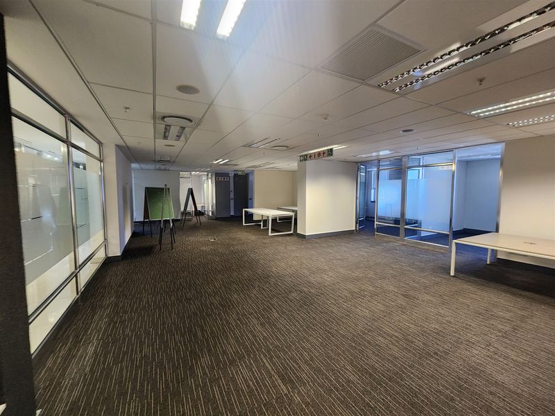 Spacious open-plan office area featuring glass partitions, suspended ceilings with recessed lighting, and neutral carpeting throughout.