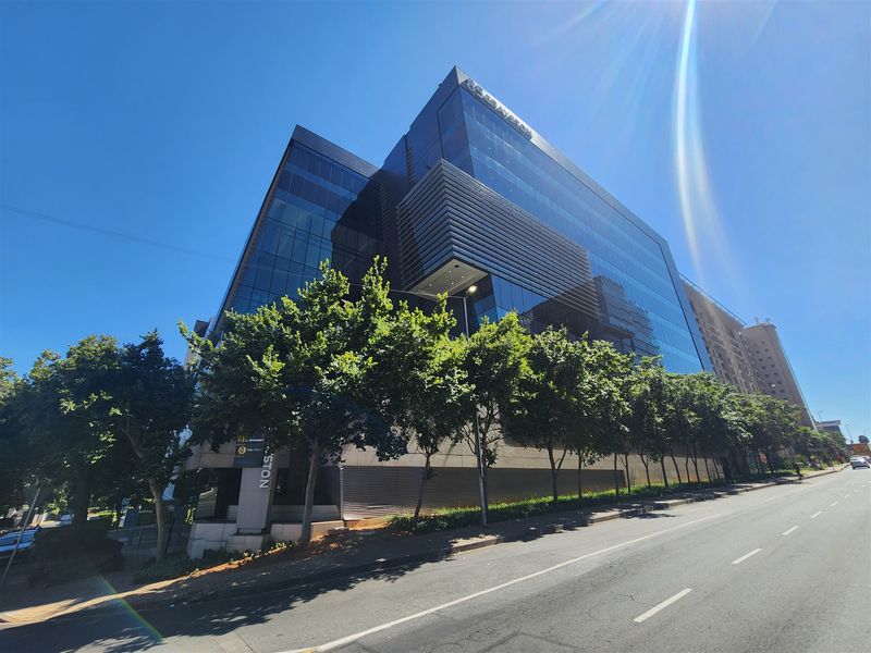 A modern multi-story commercial office building featuring a sleek glass facade and professional architectural design, situated along a paved street.