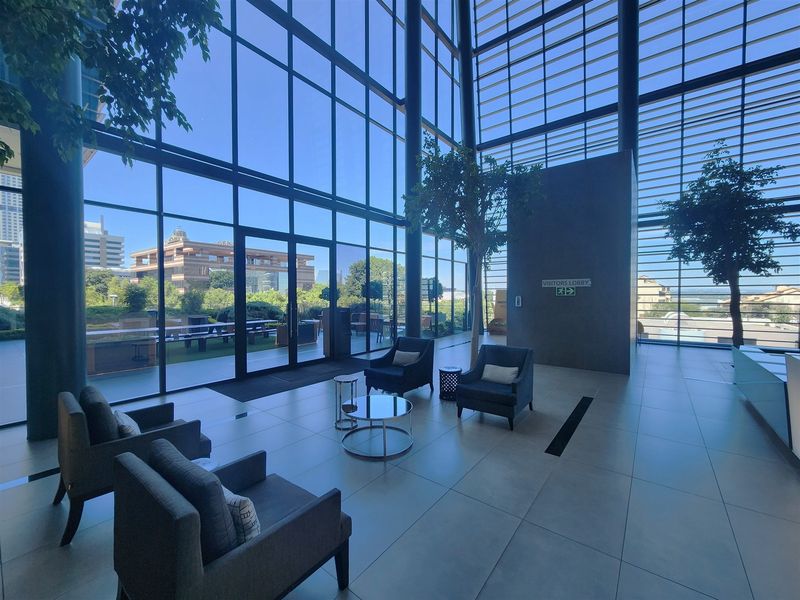 Modern office lobby featuring expansive floor-to-ceiling glass walls, high ceilings, and polished large-format floor tiles with direct access to an outdoor terrace.