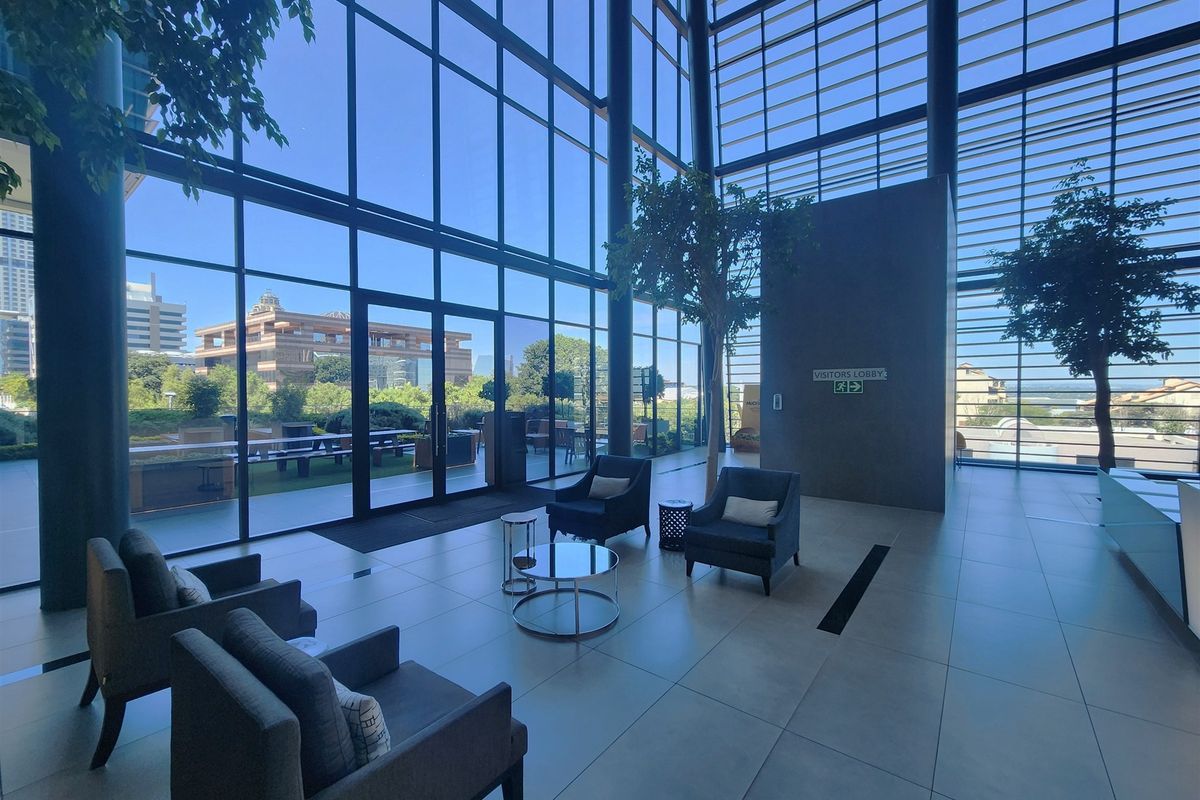 Modern office lobby featuring expansive floor-to-ceiling glass walls, high ceilings, and polished large-format floor tiles with direct access to an outdoor terrace.