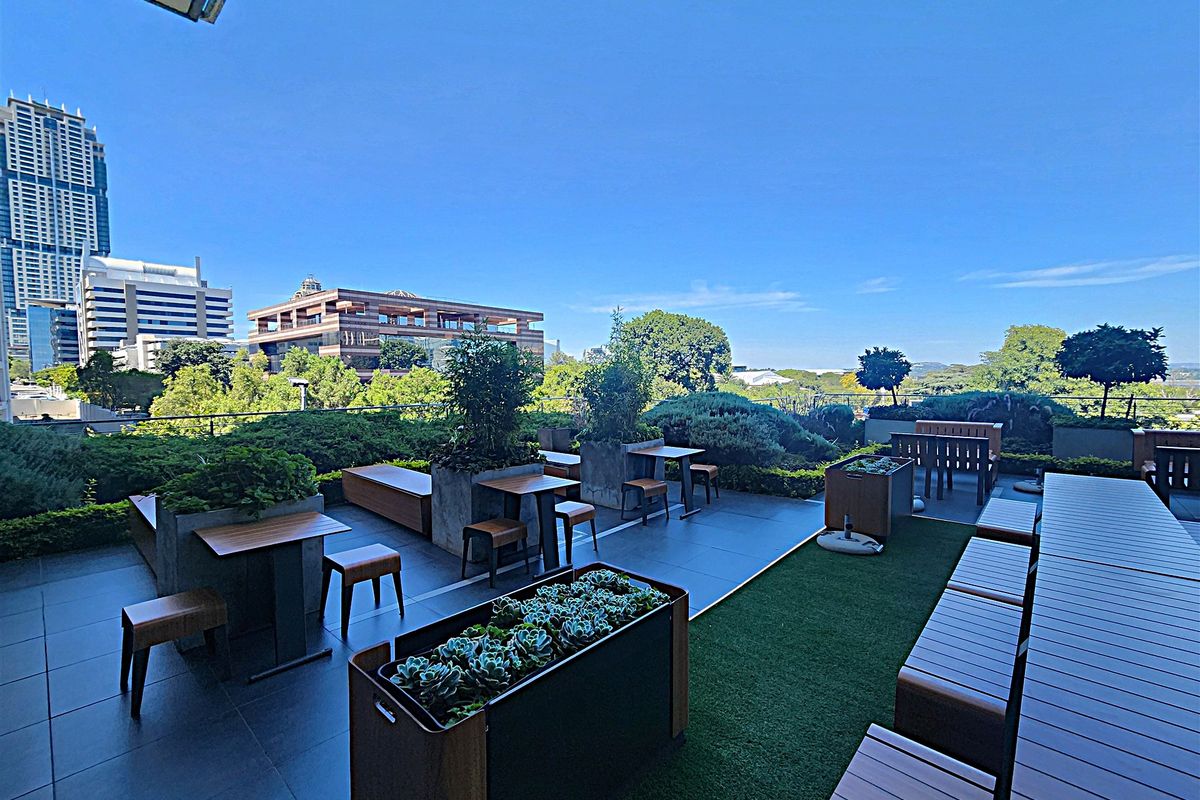 A spacious, well-maintained outdoor terrace featuring tiled flooring, artificial turf sections, built-in planters, and a glass balustrade with expansive city views.