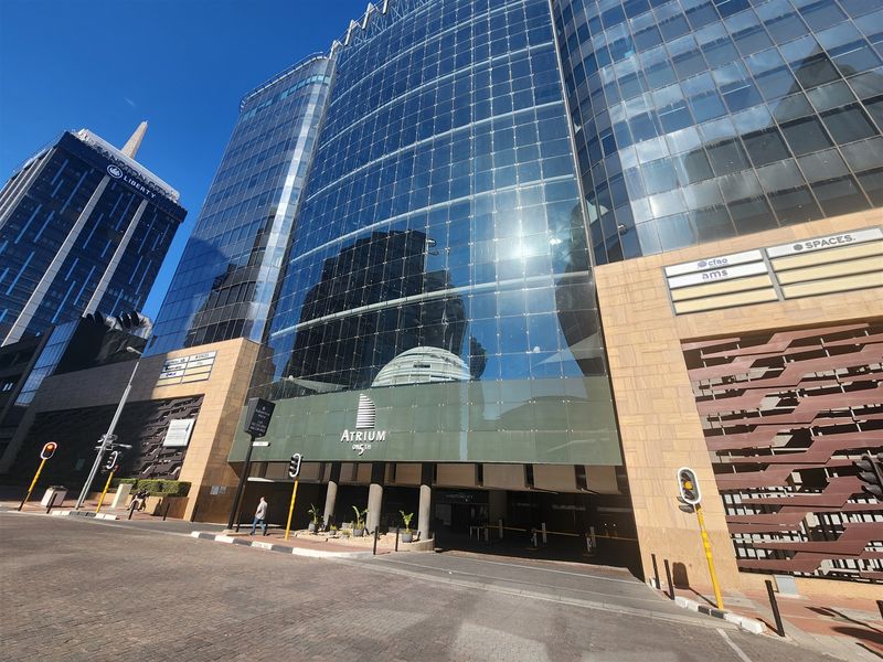 Modern commercial office building facade featuring a glass curtain wall, stone cladding, and a secure vehicle entrance.