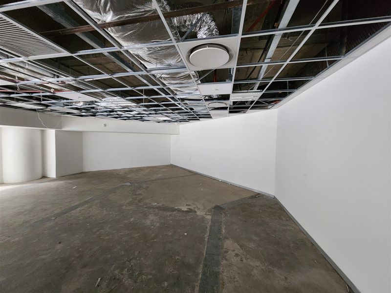 An unfinished open-plan office space featuring an exposed ceiling grid, exposed ductwork, and raw concrete flooring, ready for custom fit-out.
