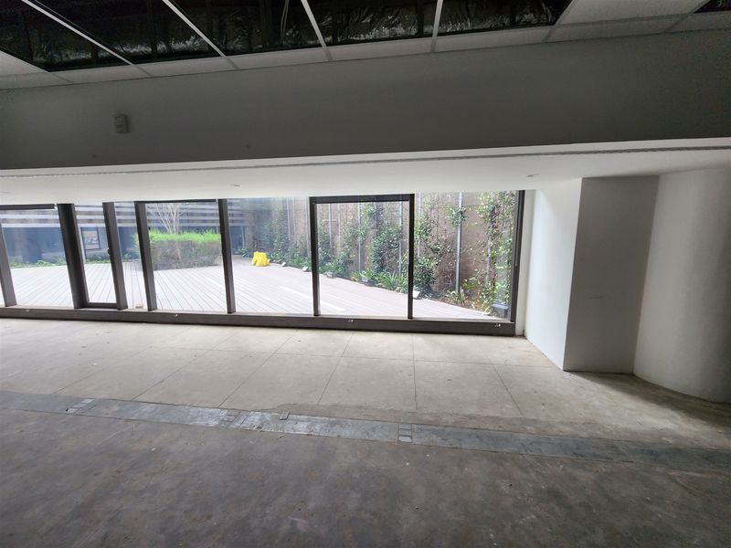 An empty office space featuring large floor-to-ceiling windows with direct access to an outdoor deck area and a suspended ceiling grid.