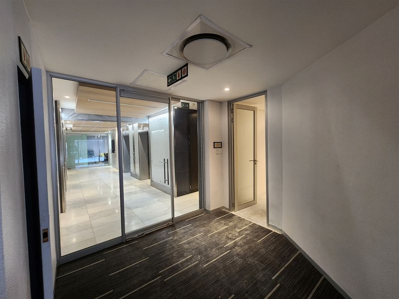 A clean, modern office hallway featuring a glass partition, tiled flooring in the elevator lobby, and carpeted transition area with recessed lighting.