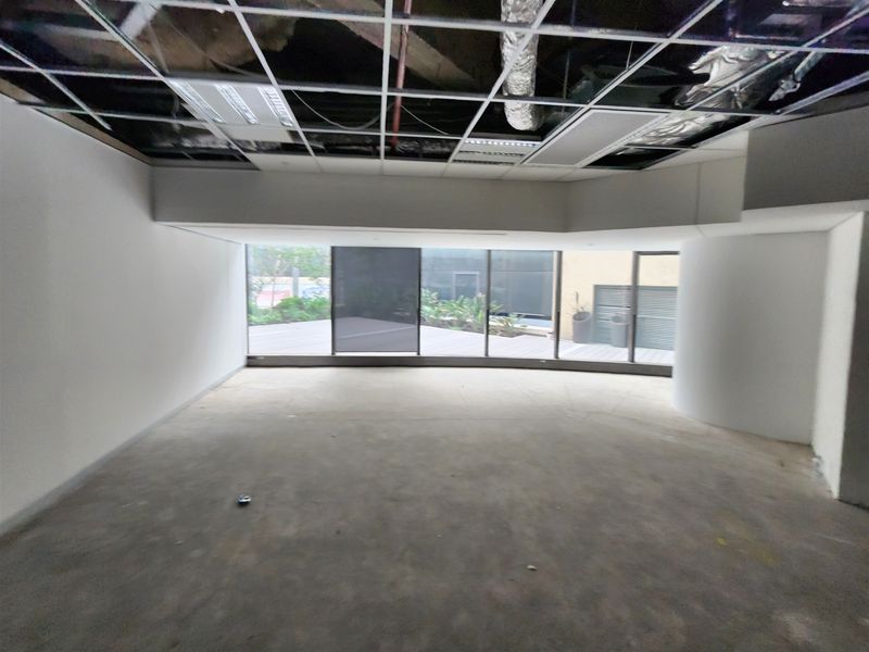 An empty office space featuring large glass doors, exposed ceiling grid, and unfinished flooring, offering a blank canvas for custom fit-out.