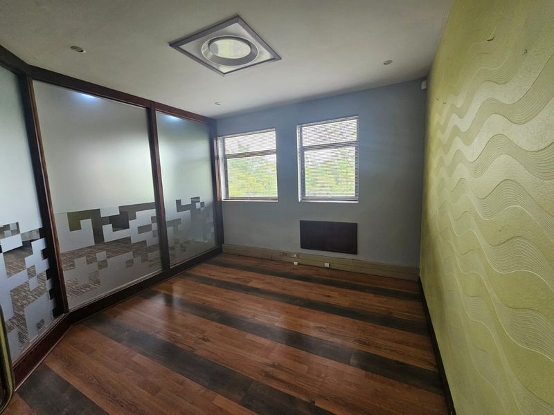 Empty office space featuring laminate flooring, a frosted glass partition, and a textured feature wall with natural light from dual windows.