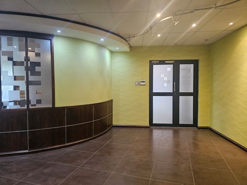 A professional office entrance featuring a curved feature wall, tiled flooring, double glass doors, and integrated lighting, providing a clean and welcoming reception area.