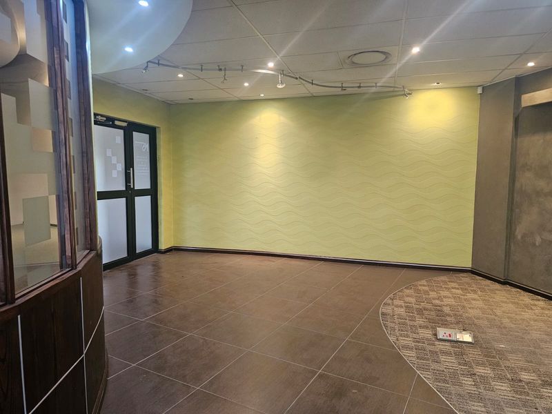 An empty office space featuring a mix of tiled and carpeted flooring, textured feature wall, track lighting, and a glass-paneled entrance door.