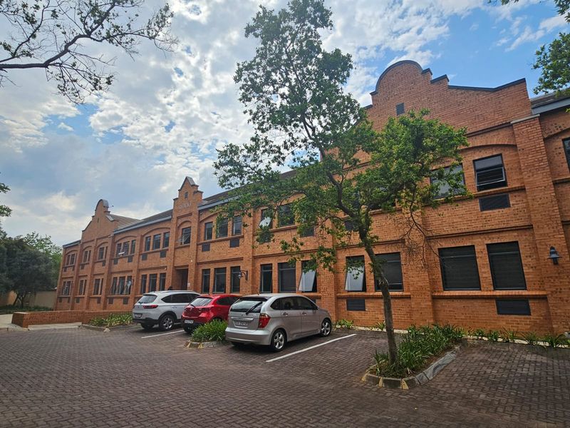 A multi-story commercial building featuring a classic red brick facade with paved parking and established landscaping in the front.