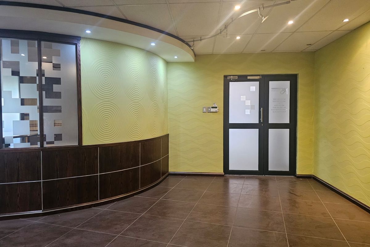 A professional office entrance featuring a curved feature wall, tiled flooring, double glass doors, and integrated lighting, providing a clean and welcoming reception area.