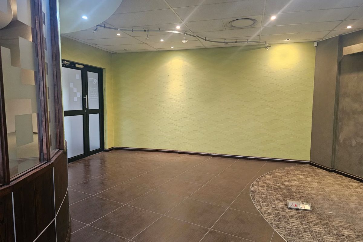 An empty office space featuring a mix of tiled and carpeted flooring, textured feature wall, track lighting, and a glass-paneled entrance door.
