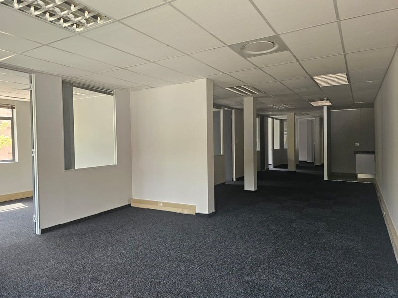 An open-plan office space featuring suspended ceilings, carpeted flooring, and glass partitions, offering a versatile layout for professional use.