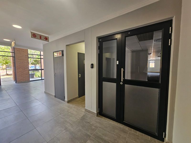 A clean, modern commercial hallway featuring tiled flooring, secure double glass entry doors, and integrated access control systems.