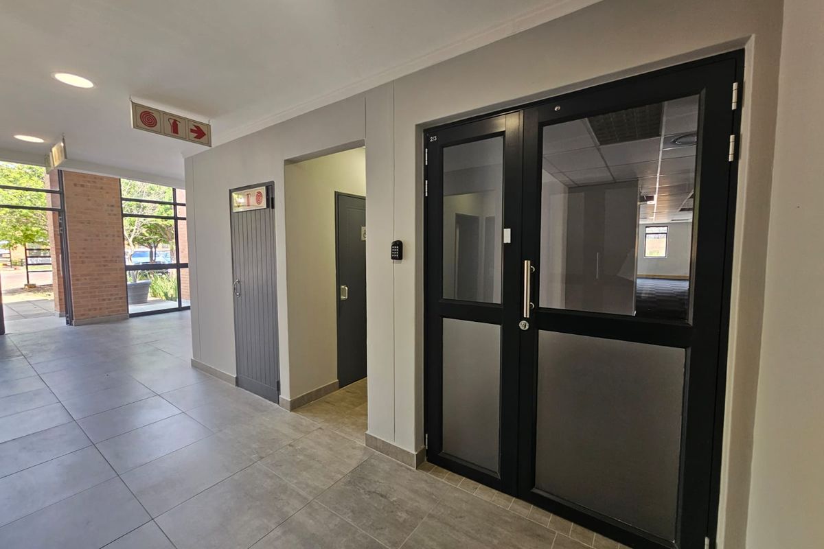 A clean, modern commercial hallway featuring tiled flooring, secure double glass entry doors, and integrated access control systems.