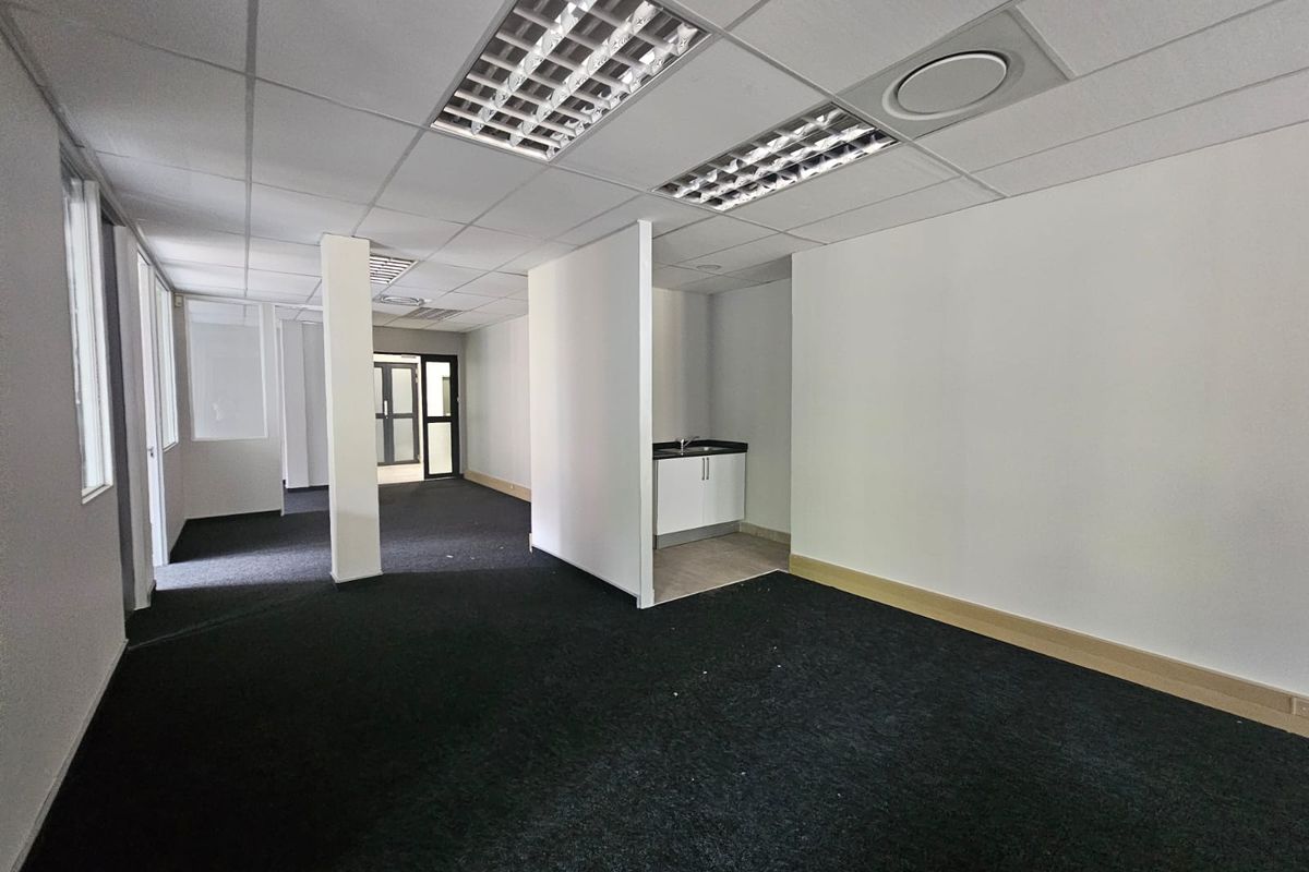 Open plan office space featuring a kitchenette, suspended ceilings with recessed lighting, and dark carpeting throughout.