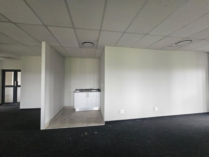 A vacant office kitchenette area featuring a small cabinet with a stainless steel sink, drop ceiling, and dark carpeting.