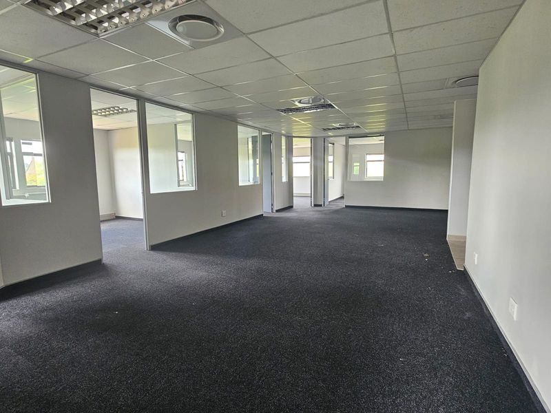 Open-plan office space featuring glass partitions, suspended ceilings with recessed lighting, and dark carpeting, offering a versatile layout for professional use.