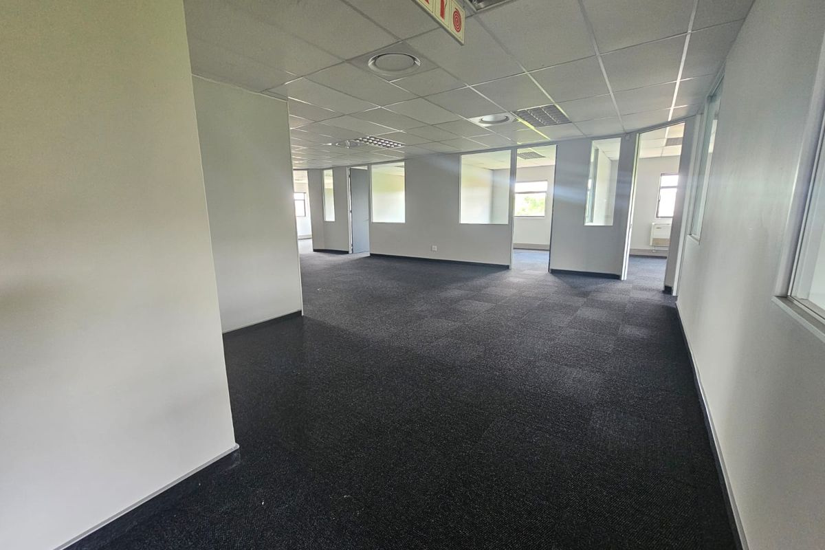 An open-plan office space featuring carpet tiles, suspended ceilings with recessed lighting, and glass partition walls creating separate work areas.