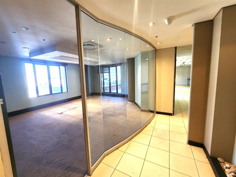 An empty office space featuring a curved glass partition wall, recessed lighting, and a combination of tiled and carpeted flooring.