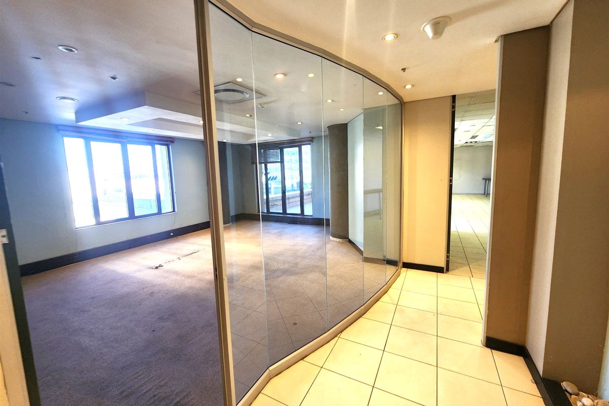 An empty office space featuring a curved glass partition wall, recessed lighting, and a combination of tiled and carpeted flooring.