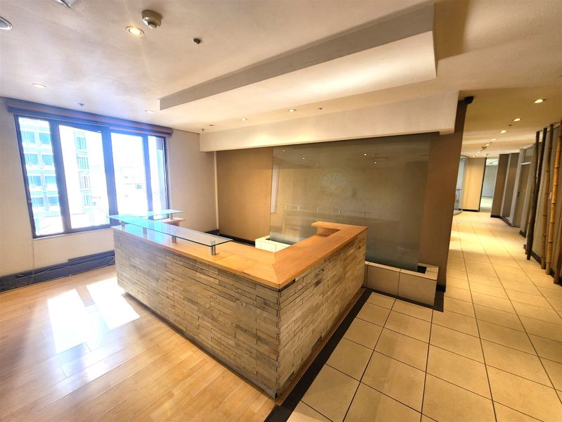 A professional office reception area featuring a built-in stone-clad desk, glass partition, and a mix of tiled and wooden flooring.