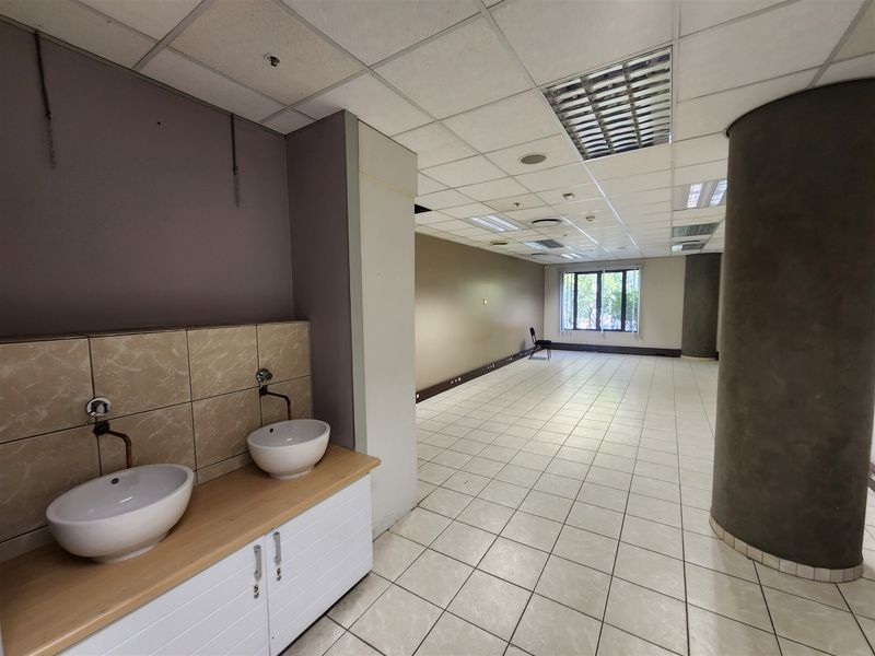 Open-plan office space featuring a built-in vanity with dual sinks, ceramic tile flooring, and a suspended ceiling with recessed lighting.