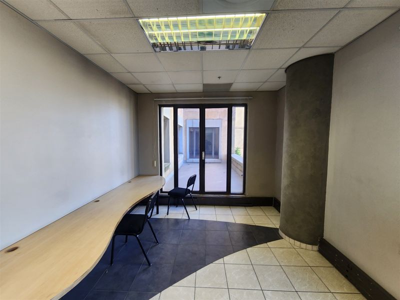 A functional office space featuring a built-in desk, suspended ceiling with recessed lighting, and direct access to an outdoor area through glass sliding doors.