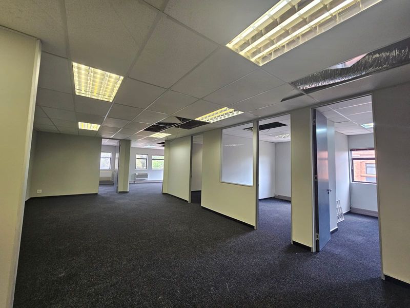Open-plan office space featuring carpeted flooring, suspended ceilings with integrated lighting, and partitioned office rooms with glass panels.