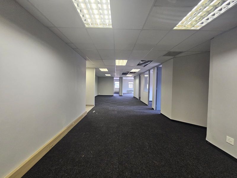 An empty, open-plan office space featuring dark carpeting, suspended ceilings with recessed lighting, and internal partitioning, requiring minor ceiling repairs.