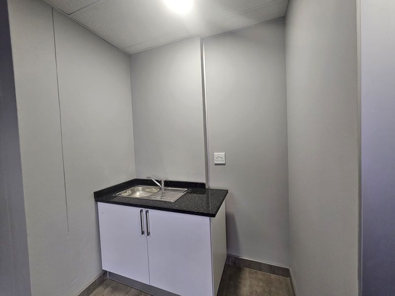 A compact kitchenette or scullery area featuring a stainless steel sink, granite countertop, and clean white base cabinetry.