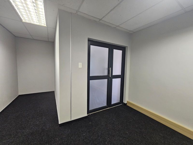 A clean, empty office space featuring dark carpeting, a suspended ceiling with recessed lighting, and a modern frosted glass double door entrance.