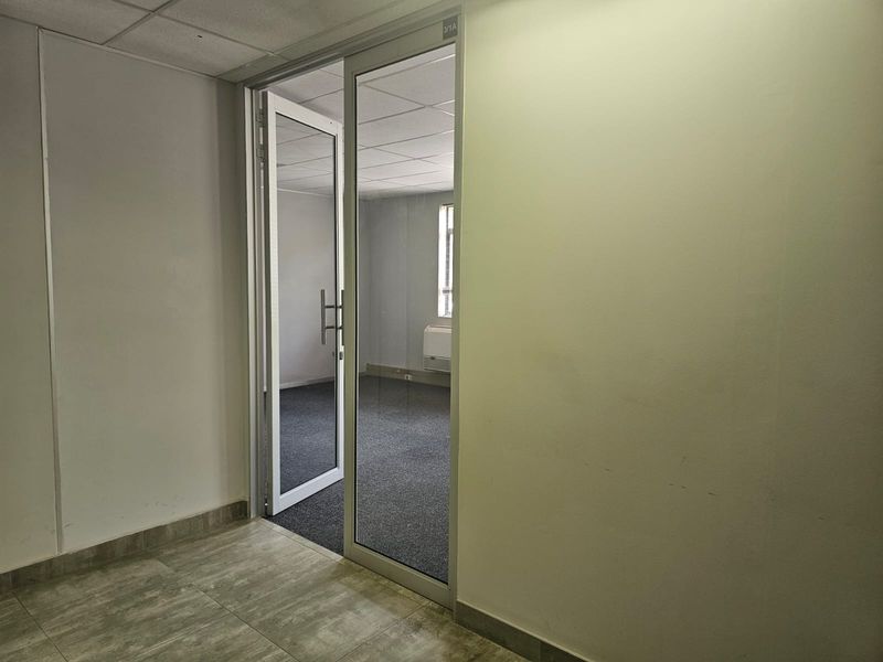 A vacant office space featuring a glass entrance door, carpeted flooring, and a suspended ceiling, providing a clean and professional environment.