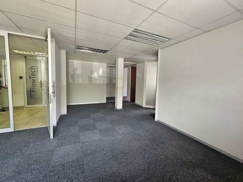 A vacant office space featuring carpet tiles, a suspended ceiling with recessed lighting, and a glass partition entrance.