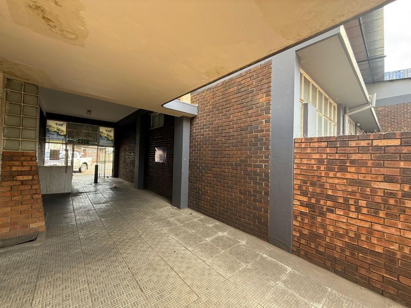 Covered entrance area featuring brick masonry, tiled flooring, and a security gate, providing a functional access point to the office property.