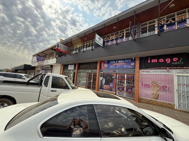 Front exterior view of a multi-tenant commercial office building featuring ground-level storefronts and an upper-level balcony with signage.