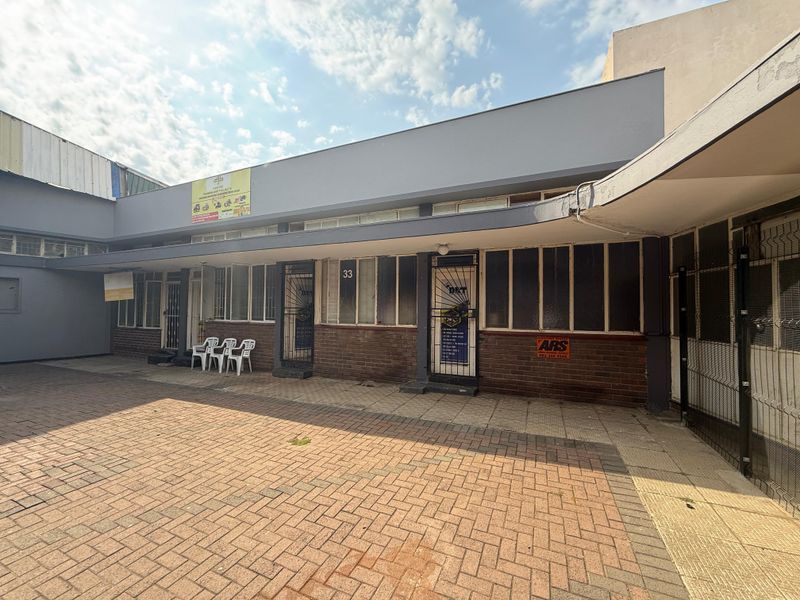 Front exterior view of a commercial office building featuring brick paving, security gates, and a covered walkway entrance.