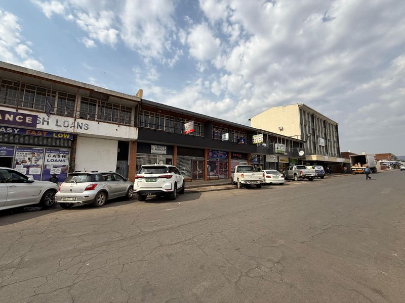 Street-level view of a multi-story commercial office and retail building featuring ground-floor storefronts and upper-level office windows along a paved road.