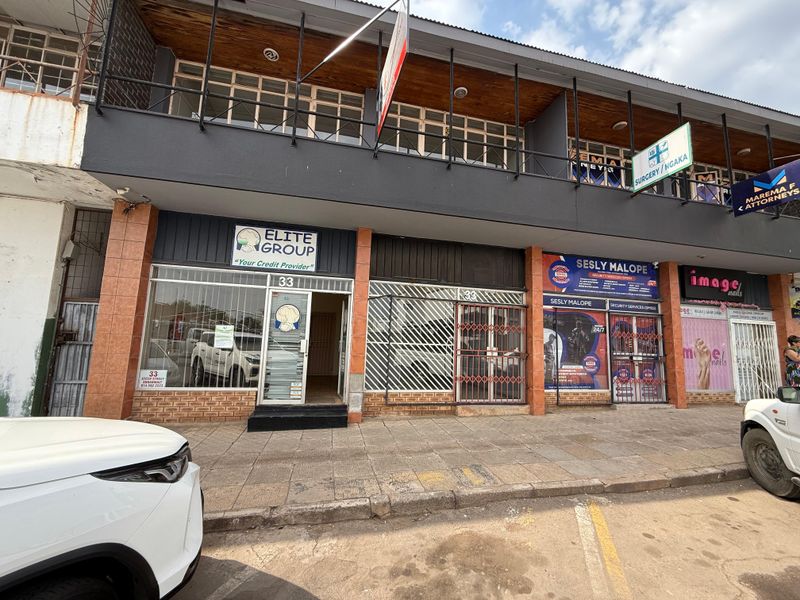 Front elevation of a multi-tenant commercial office building featuring glass storefronts, security gates, and upper-level balcony access.