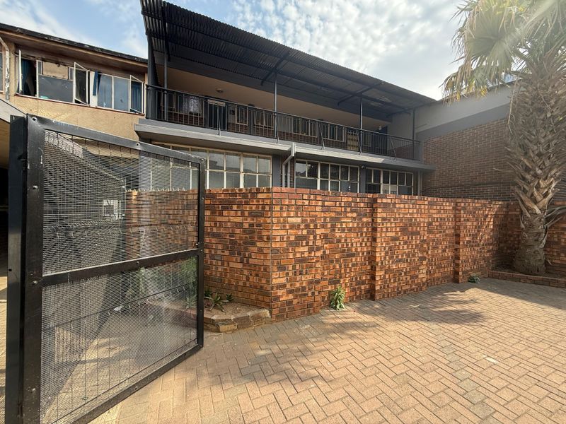 Rear exterior view of the office building featuring a paved courtyard, brick boundary wall, secure metal gate, and a covered upper-level balcony.